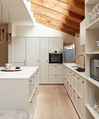 white modern kitchen with white cabinetry, beamed ceiling, wooden flooring, wooden knobs on units, white countertop