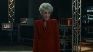 Anita Dobson's Mrs. Flood dressed in red coat