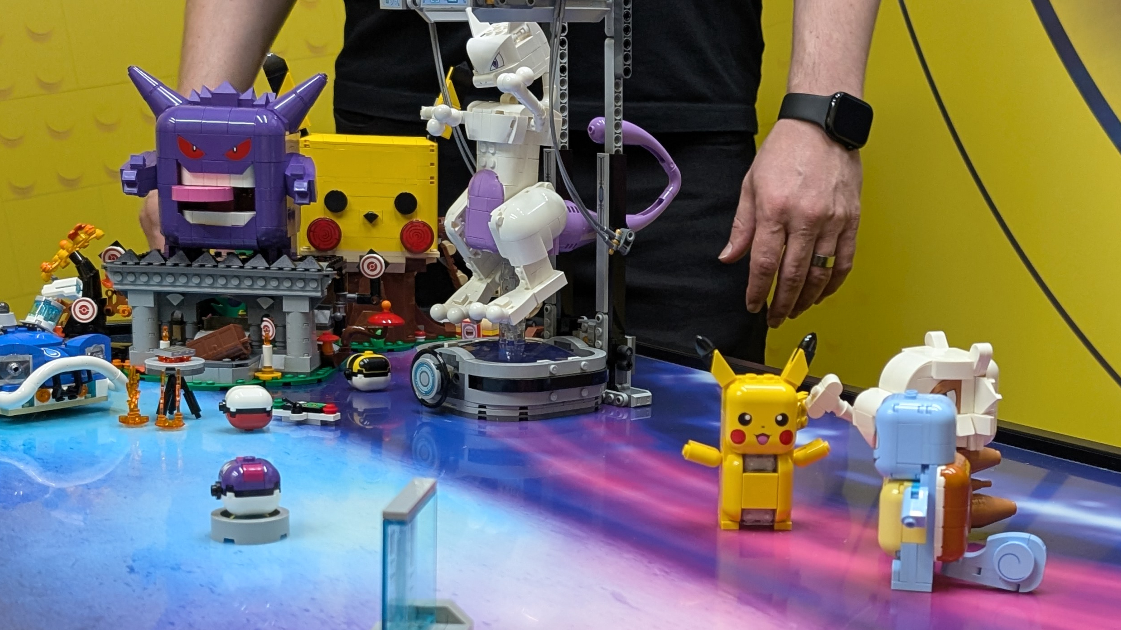 Lego Pokemon laid out on a blue and purple surface, with a person wearing black visible behind them