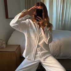 Woman in mirror takes photo wearing white shit and white trousers
