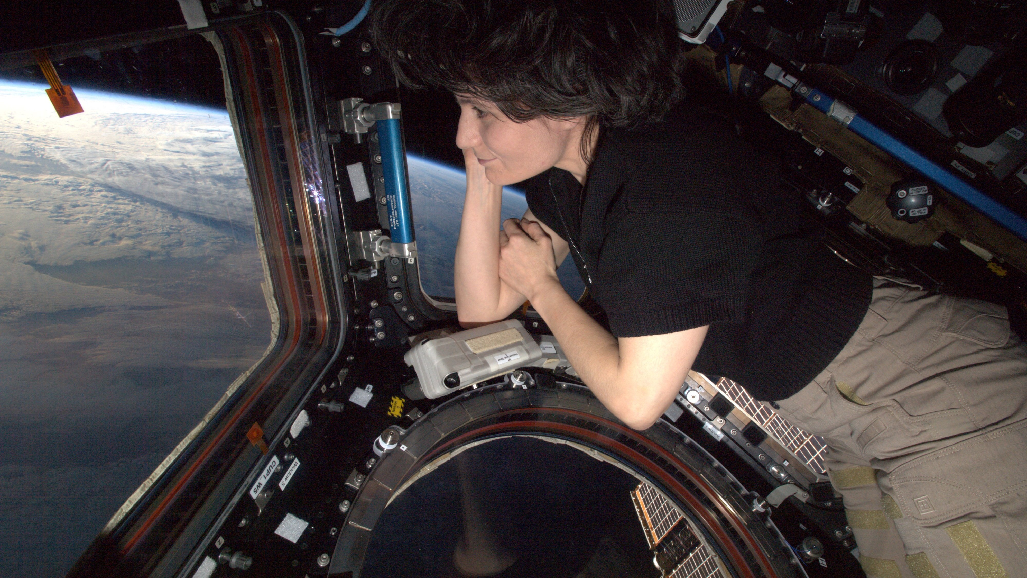 samantha cristoforetti leaning on cupola and looking outside with a view of earth below