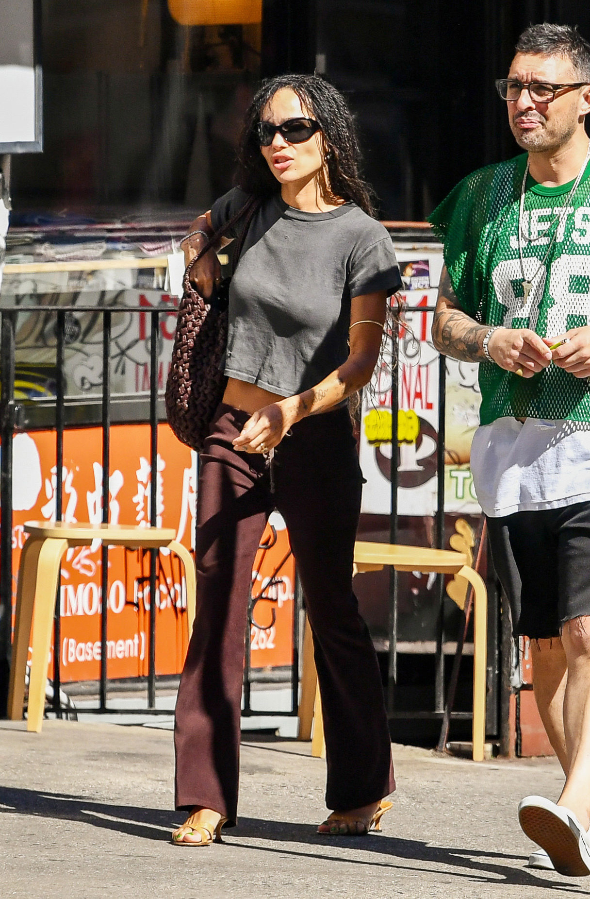 An image of Zoe Kravitz wearing suede bootcut jeans with beige heels, a grey T-shirt and woven leather bag.