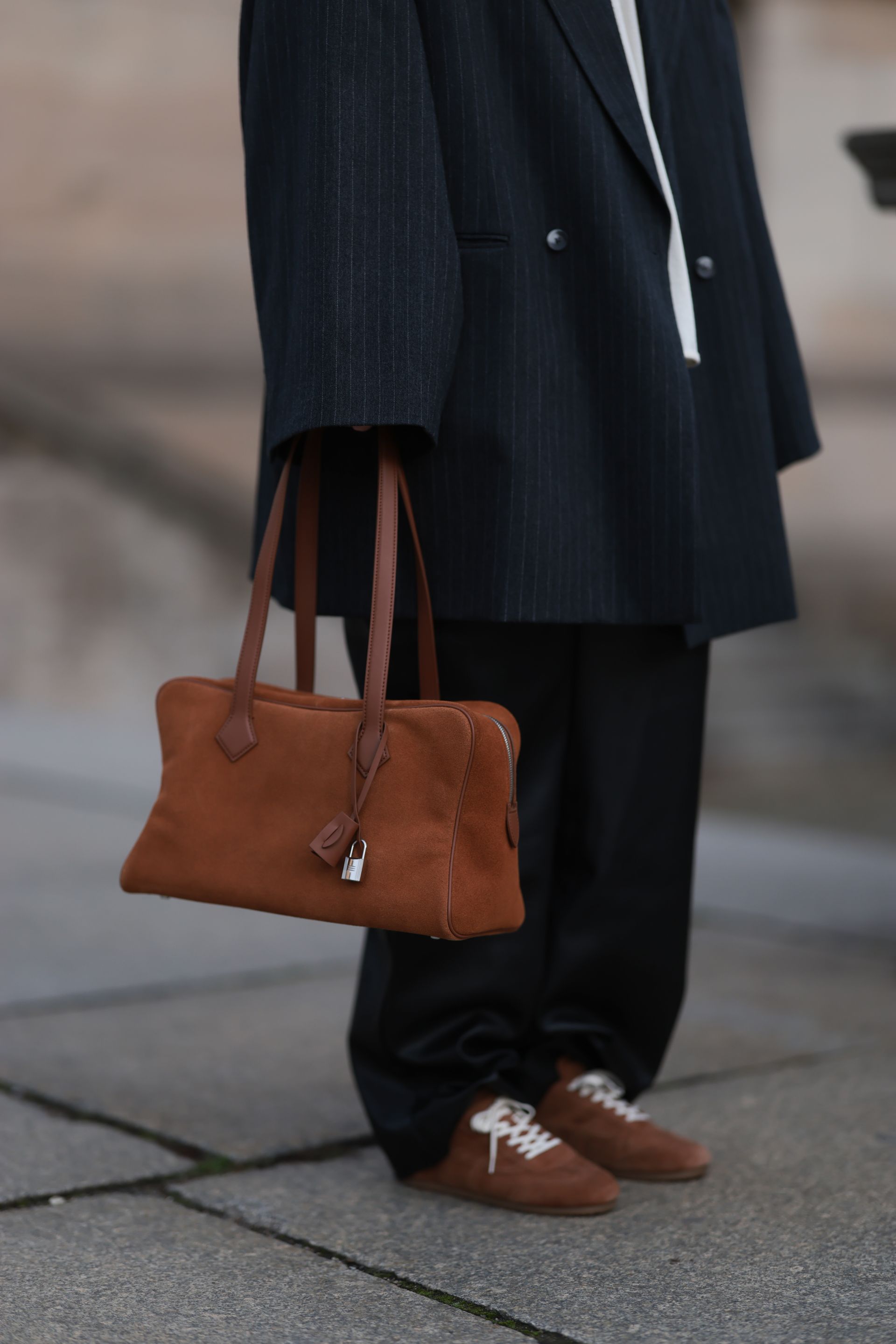 Maria Barteczko, with a dark brown straight bob haircut, seen wearing a gray striped oversized wide-fit blazer by Vival.Studio layered over a beige V-neck knitted sweater from Gitta Banko The Label. She completes the look with black wide-fit leather pants by The Frankie Shop and brown suede leather sneakers from COS. The outfit is accessorized with a vintage brown suede leather Victoria bag by Hermès and oversized black aviator optical eyeglasses by Victoria Beckham on October 31, 2025 in Berlin, Germany.