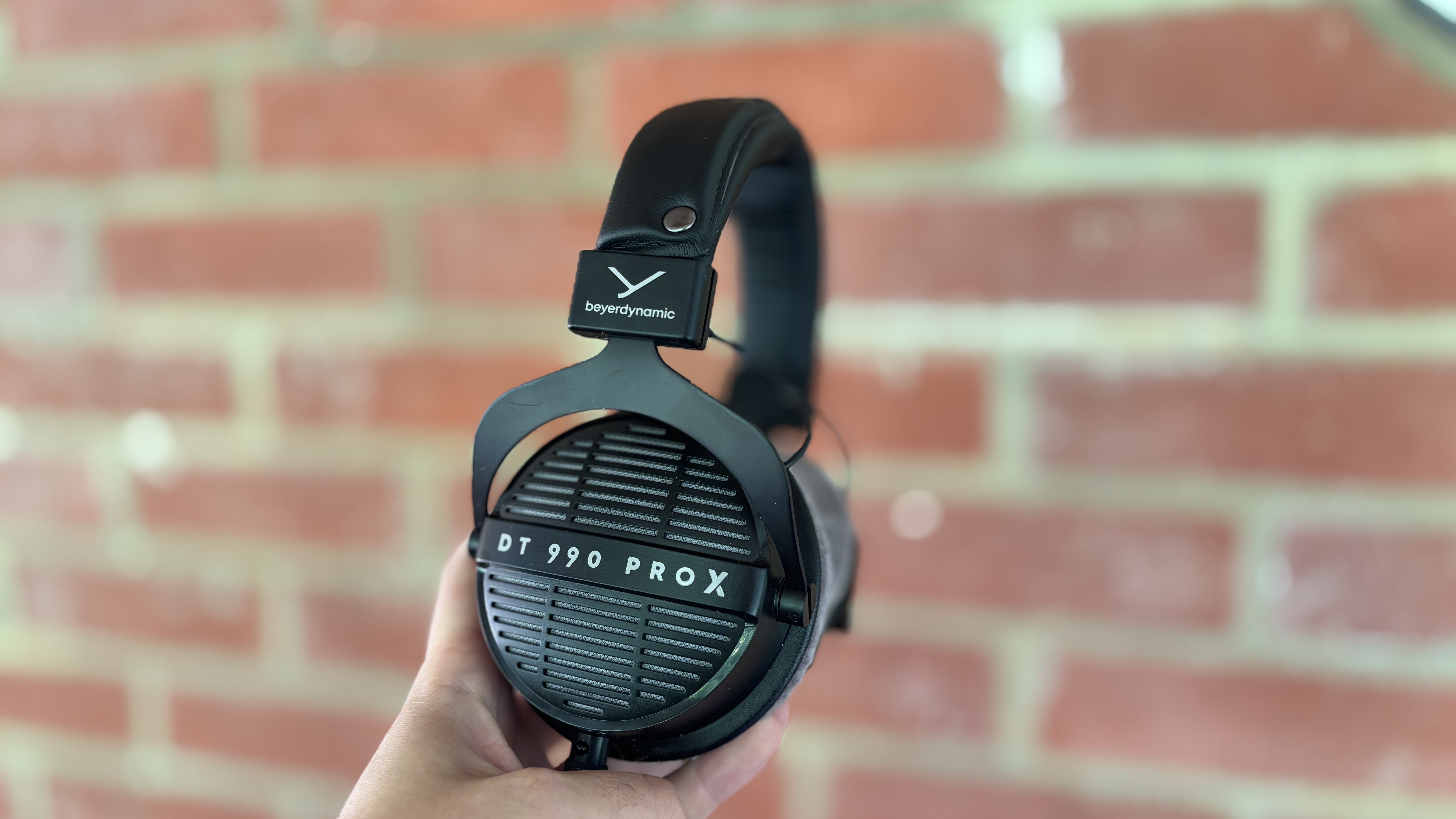 Beyerdynamic DT 990 Pro X headphones held up against brick wall