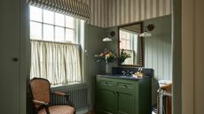 A green paneled powder room with striped wallpaper ceiling