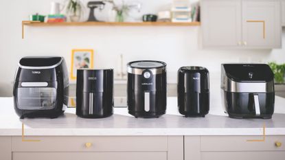 Five black air fryer models lined up along a white marble kitchen counter