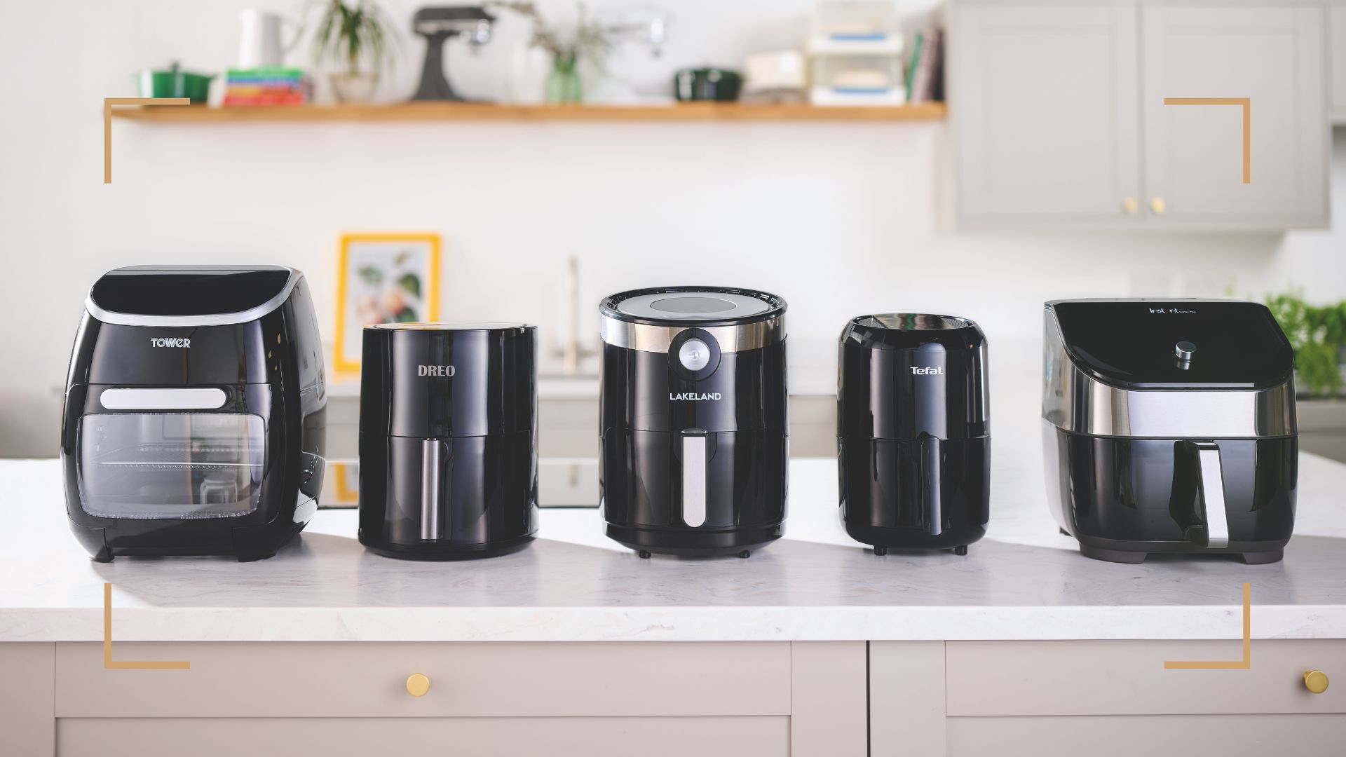 Five black air fryer models lined up along a white marble kitchen counter
