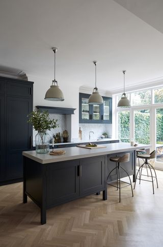 A long kitchen island with dark grey cabinets with two stylish bar stools underneath three pendant lamps