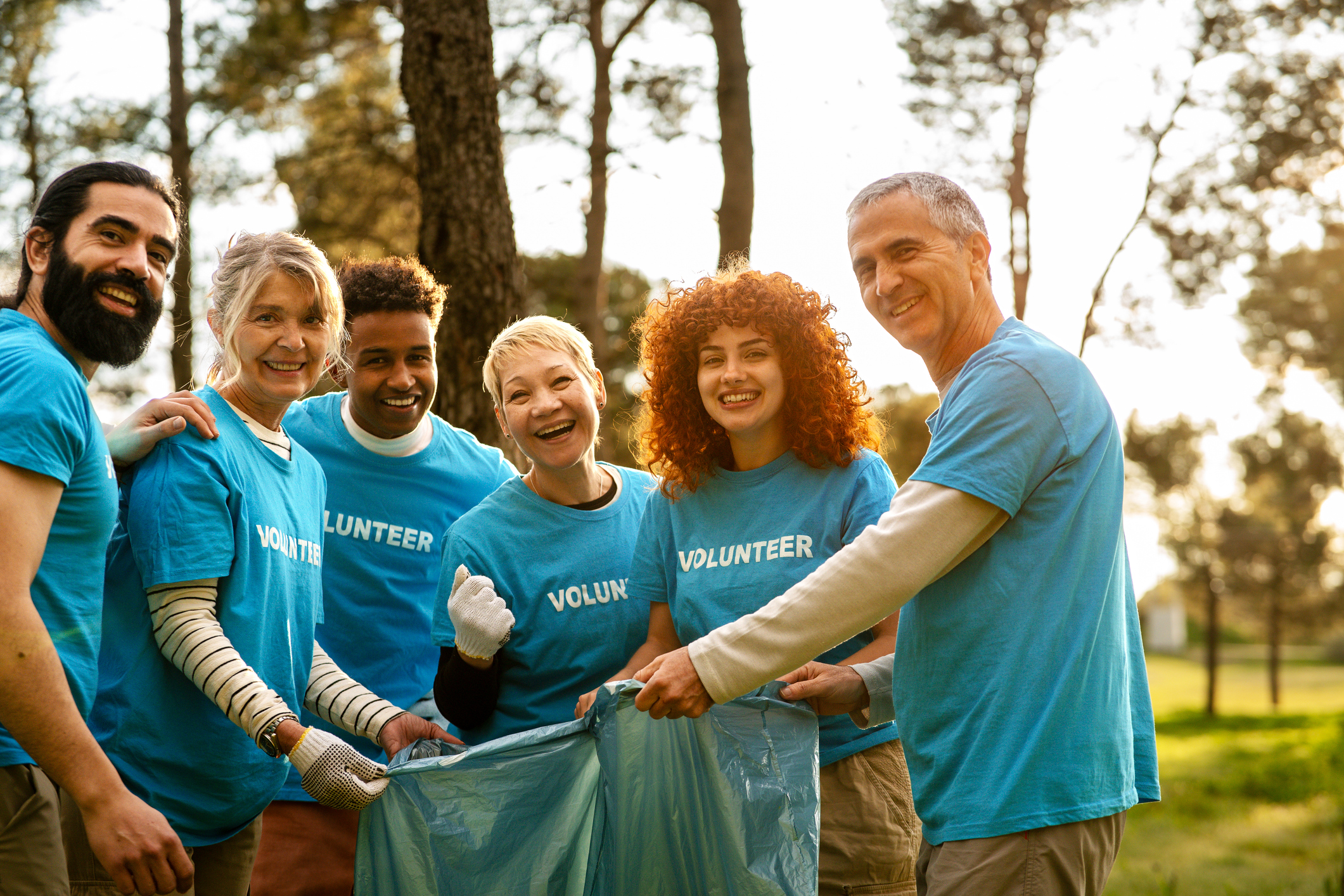 Community volunteers in matching blue shirts cleaning park, picking up litter and sharing positive teamwork spirit during environmental cleanup