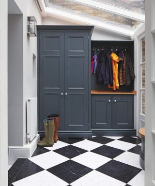 Boot room with built in cupboards and rail with coats, black and white tiled floor.