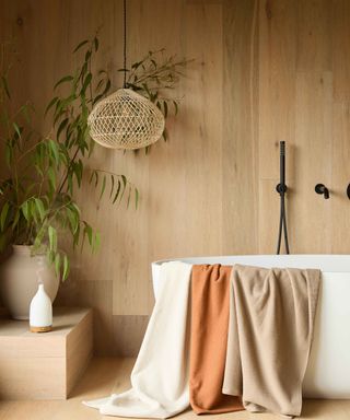 wooden bathroom wall with white freestanding bath and black brassware