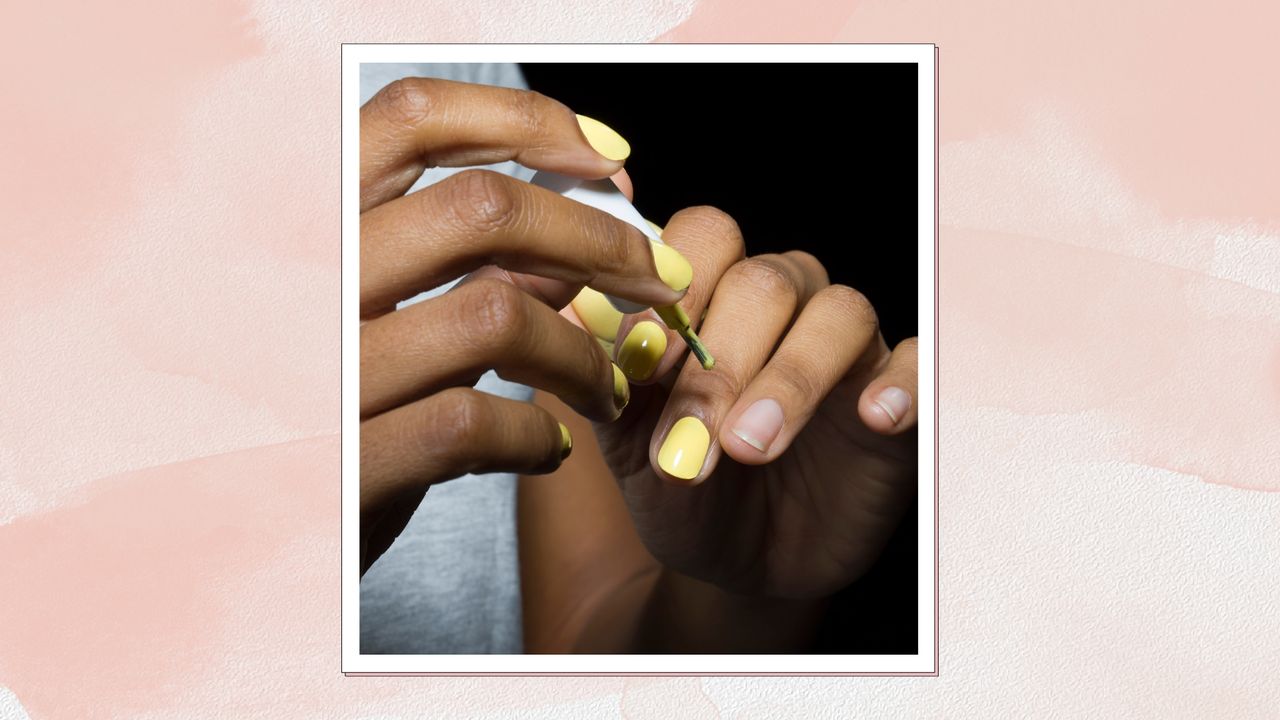 A close up of someone painting their nails with a pastel yellow nail polish, similar to the yellow shade of the &#039;Butter nails&#039; trend/ in a pastel pink watercolour-style template