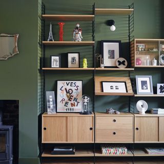 Living room with green painted wall, natural wood shelving unit decorated with books and decorations
