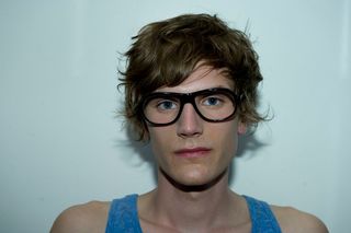 Male model with blue vest, wavy textured hair and dark framed glasses