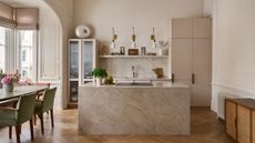 A modern kitchen with a large stone island, taupe cabinetry, and a dining table with green chairs