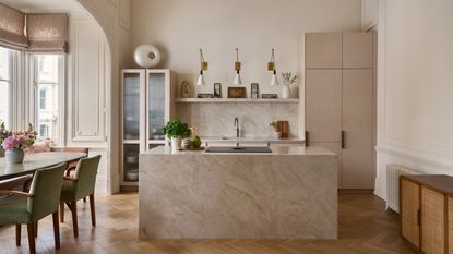 A modern kitchen with a large stone island, taupe cabinetry, and a dining table with green chairs