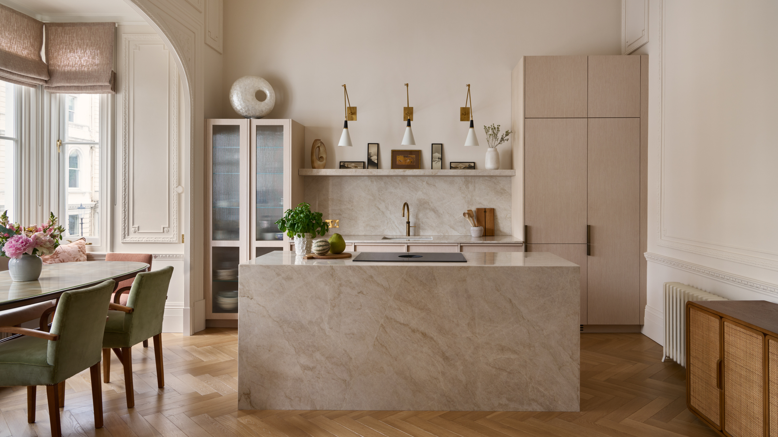 A modern kitchen with a large stone island, taupe cabinetry, and a dining table with green chairs