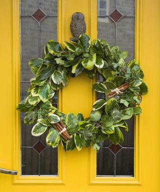 Foliage wreath with glitter and cinnamon sticks on yellow front door with owl knocker