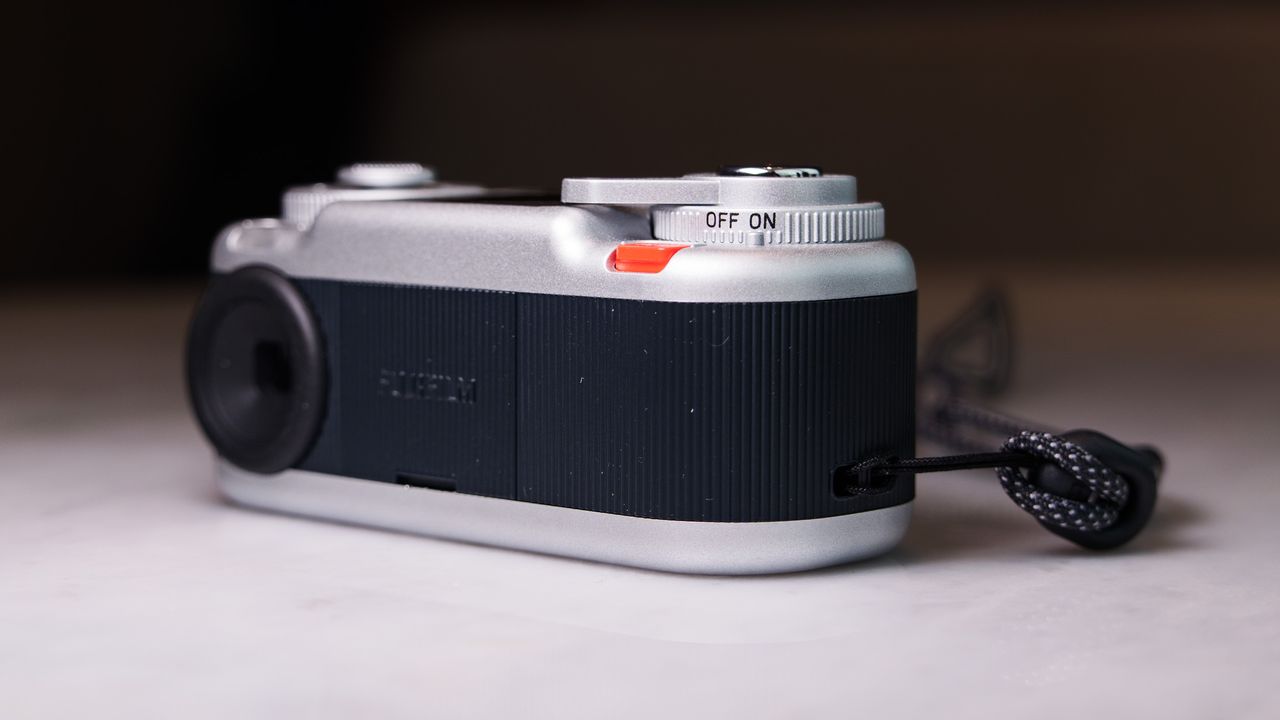 Fujifilm Instax Pal 2 digital camera on a marbled white surface, close up of the on/off switch