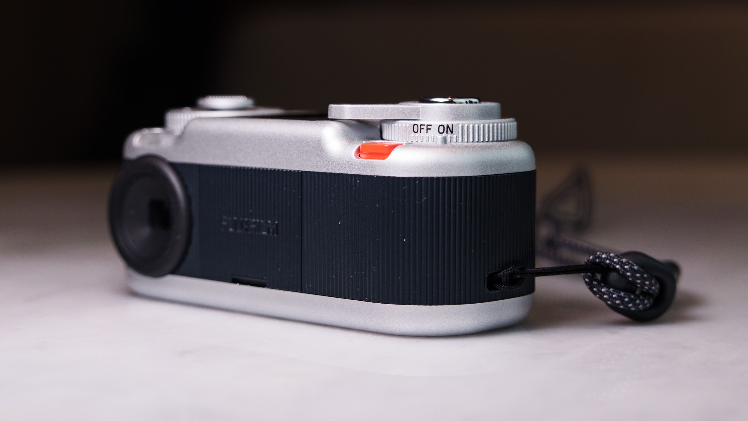 Fujifilm Instax Pal 2 digital camera on a marbled white surface, close up of the on/off switch
