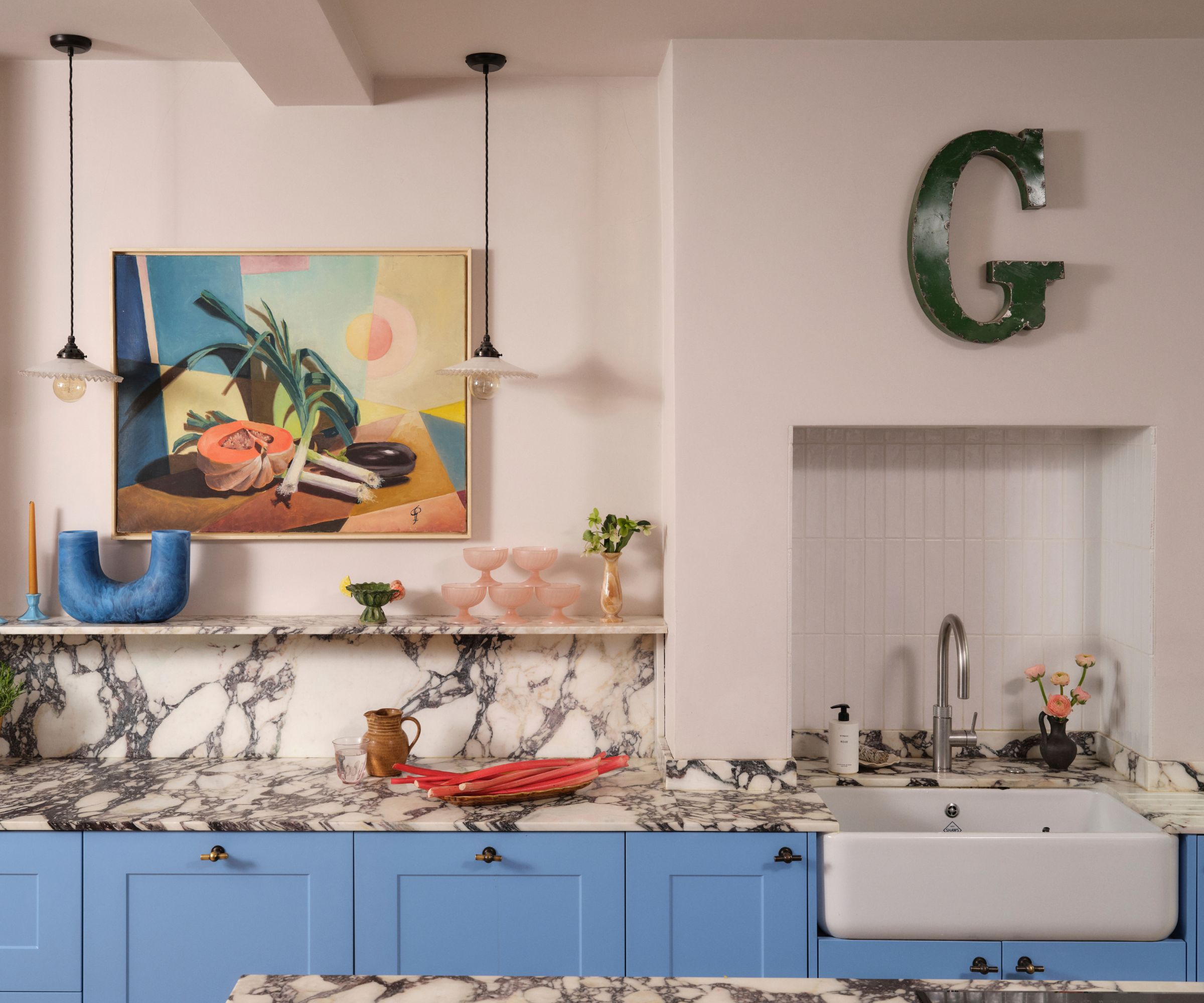 A colorful kitchen with sky blue cabinets, light pink walls, and strongly veined marble countertops