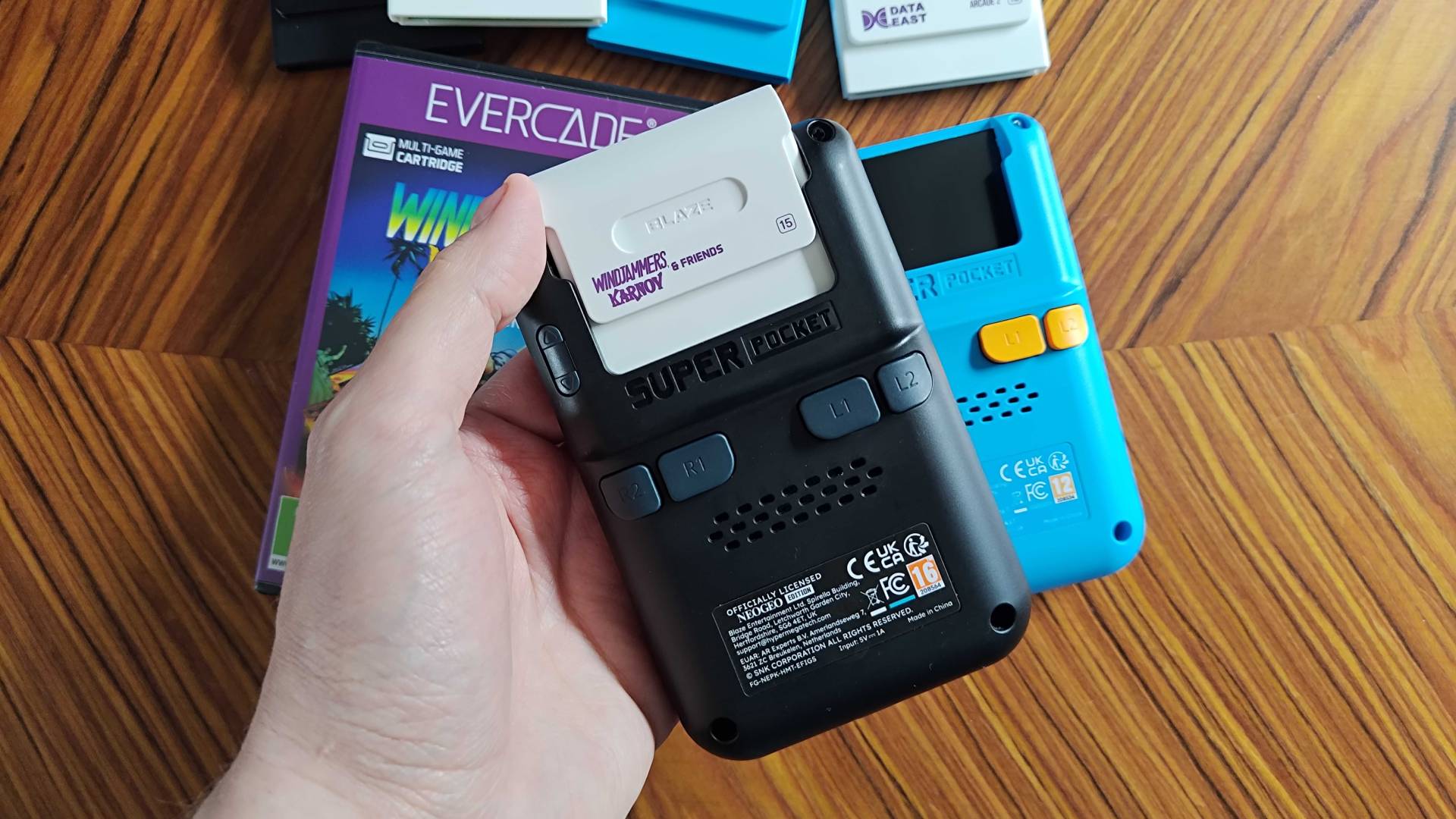 Back of Neo Geo Super Pocket with hand inserting white cartridge.