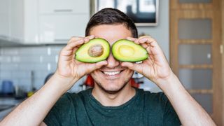 Man holds two halves of an avocado up to his eyes