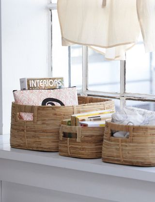 three natural woven baskets side by side on a windowsill holding books 