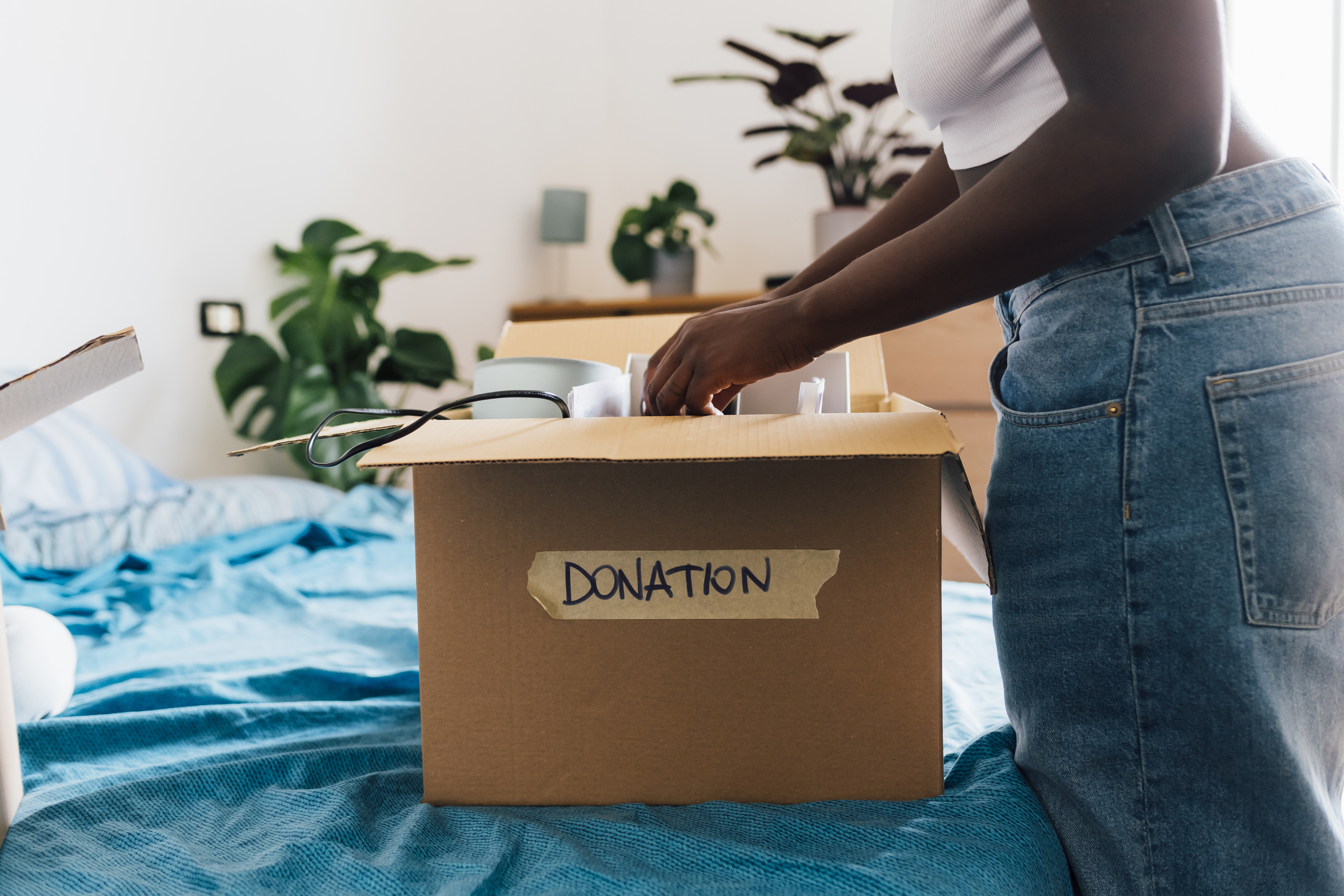 box on bed marked donations with female putting items into it