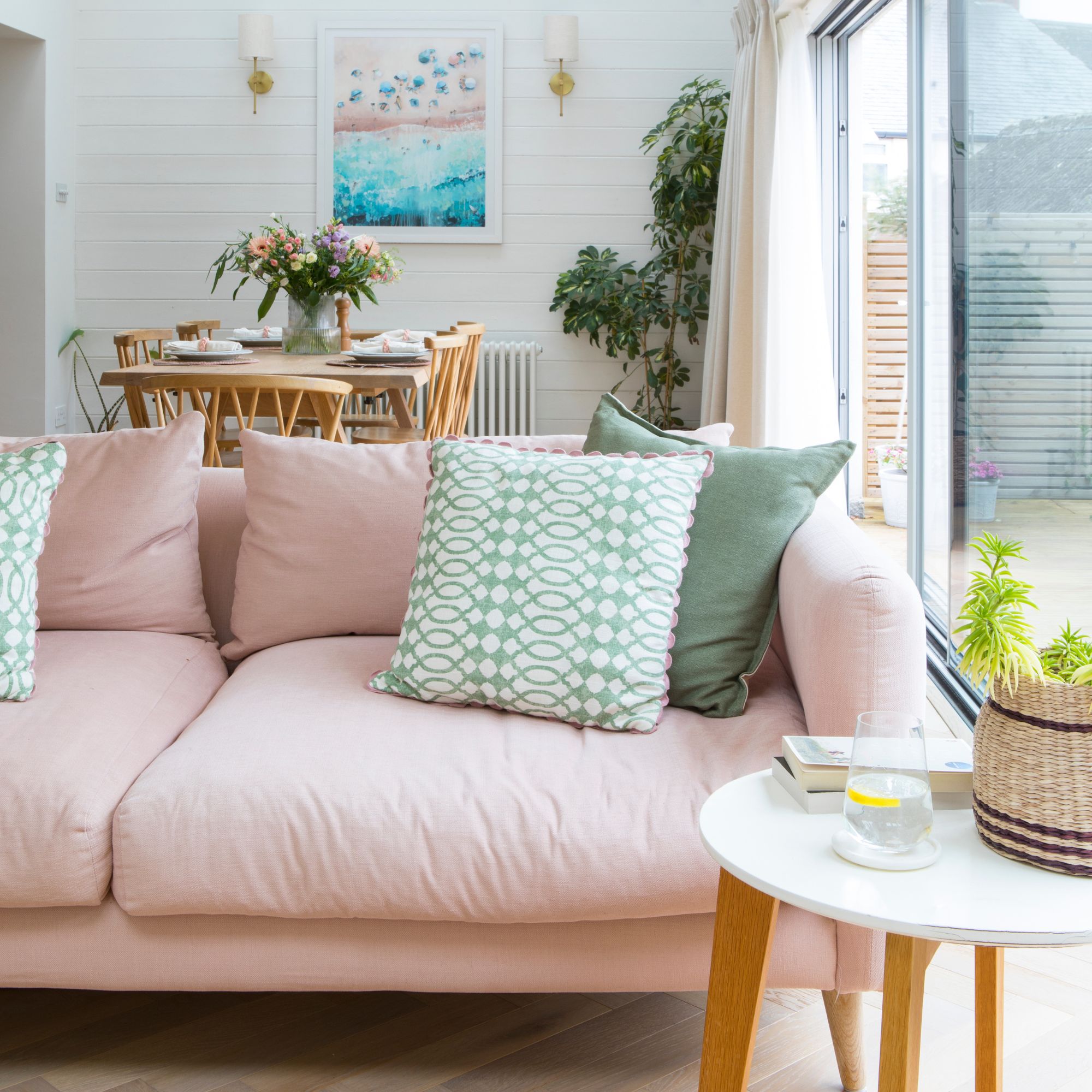 White open-plan living and dining room with a pink sofa and a wooden dining set behind it