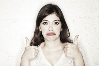 A woman holds two "thumbs up" signs, but looks unhappy.