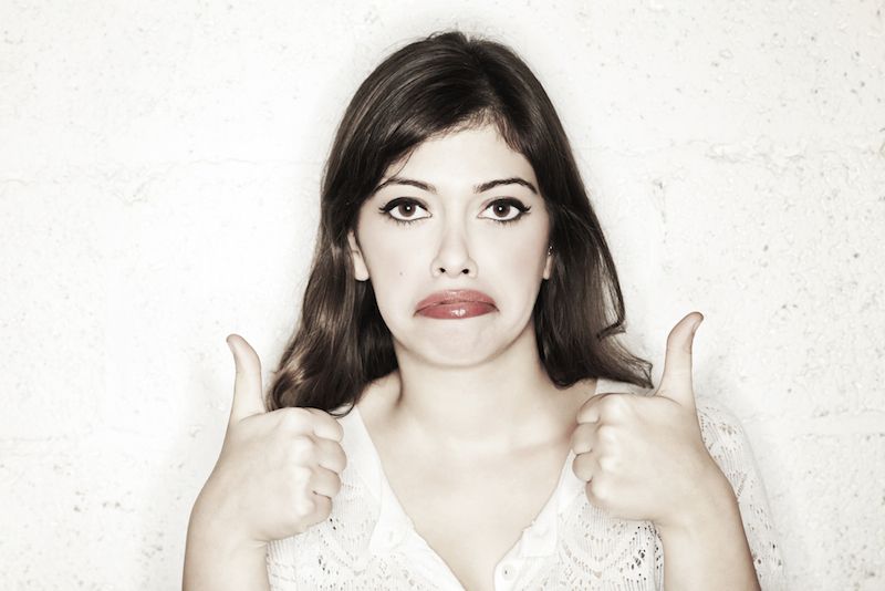 A woman holds two &quot;thumbs up&quot; signs, but looks unhappy.