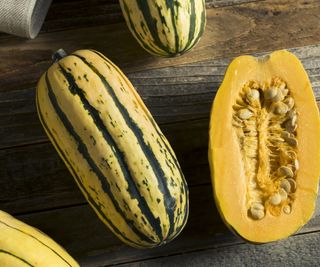 A whole delicata squash and a cut open one on a wooden board