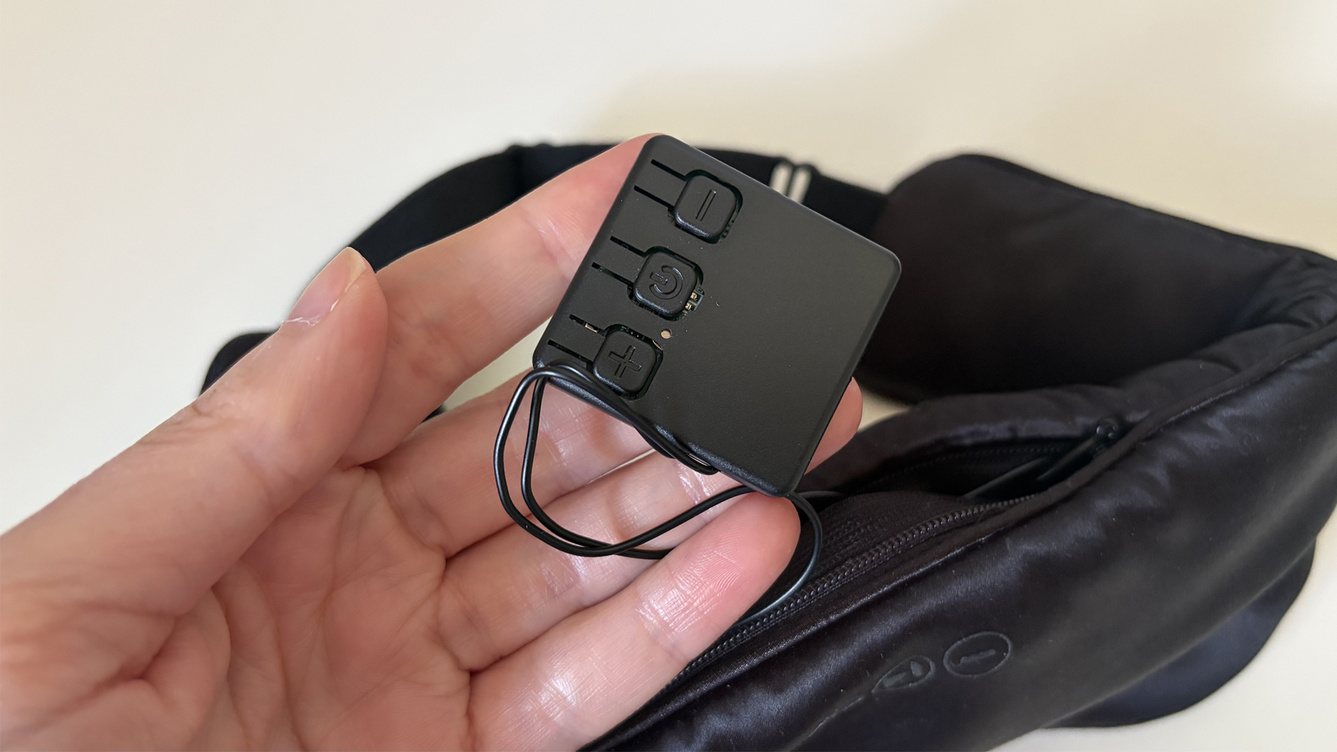 A hand holding the inner control panel, removed from the SilkSound Sleep Mask, which you can see in the background