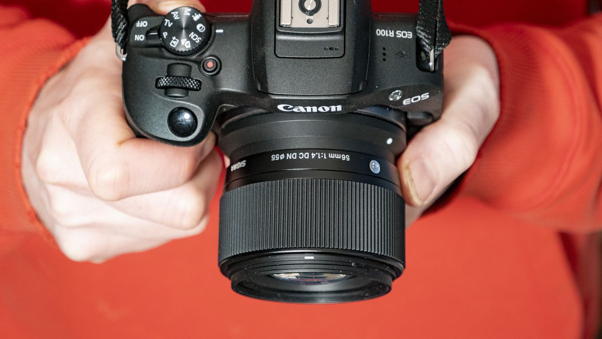 Sigma 56mm F1.4 DC DN Contemporary lens in the hand attached to a Canon EOS R100