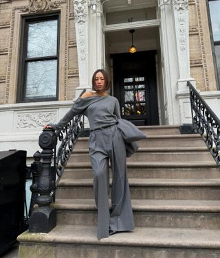 @aimeesong wears a grey draped shirt with matching pleated wide-leg trousers on the stoop of a town house in New York.