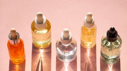 From above bottles with various moisturizing products arranged in line on pink background