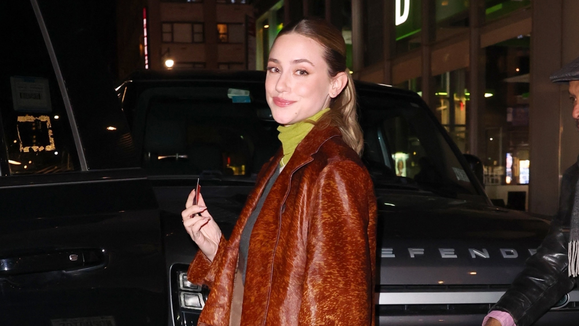 Lili Reinhart wearing a leather coat, jeans, and green accessories