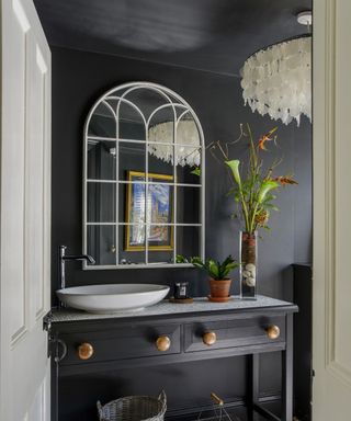 A black painted powder room with a mother of pearl chandelier