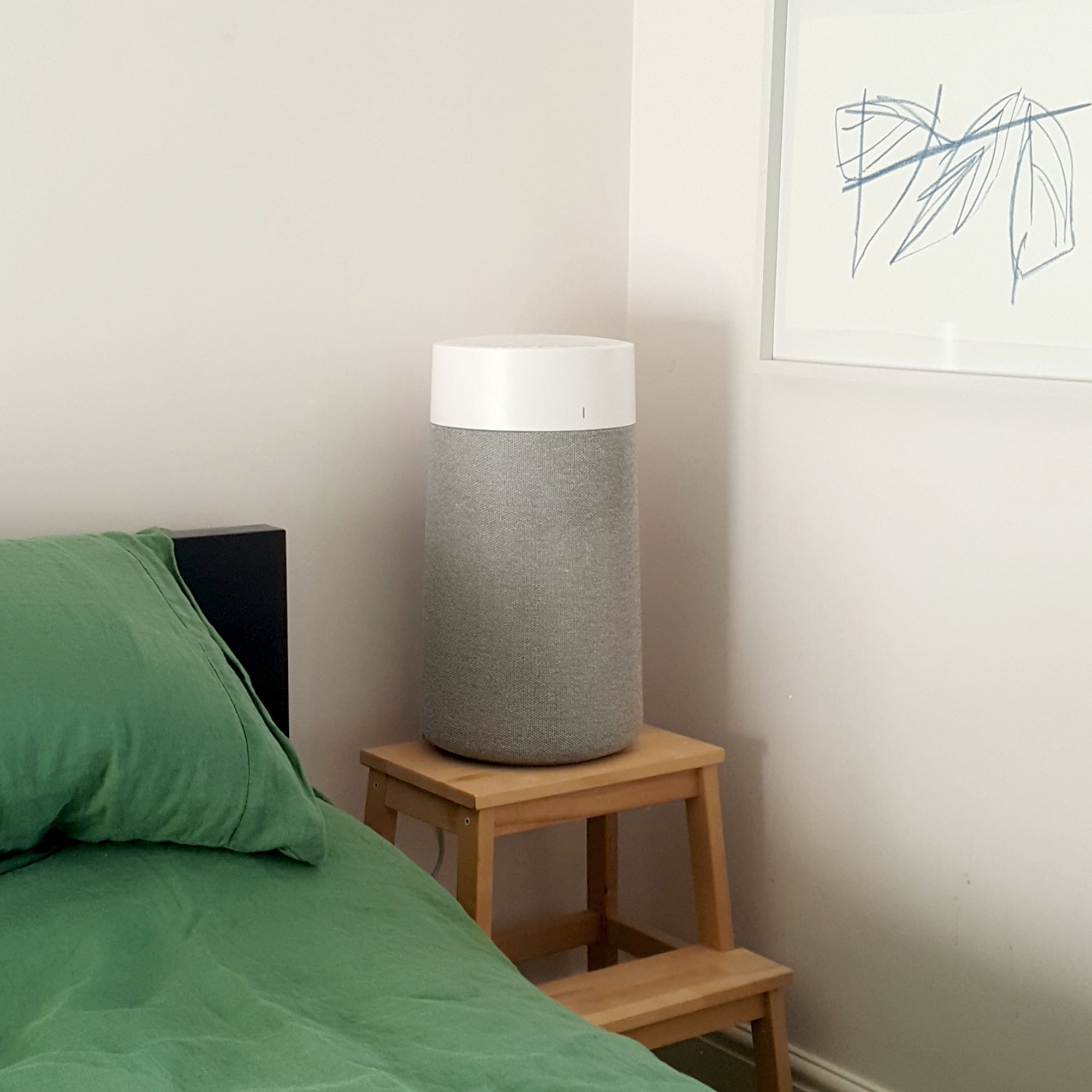 The Blueair Blue Max 3250i Air Purifier by the side of a bed with green linen bedding