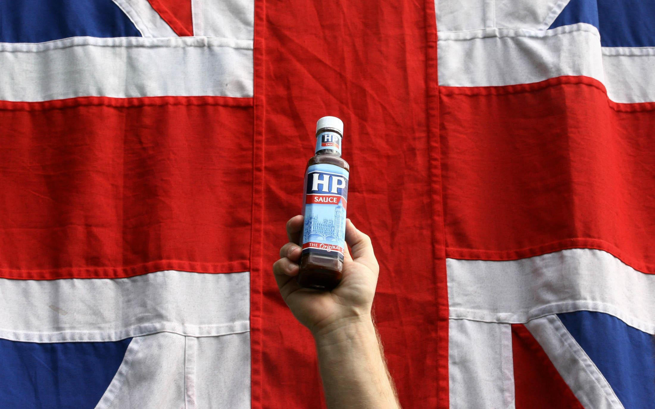 A hand holds up a bottle of HP Sauce in front of a union jack