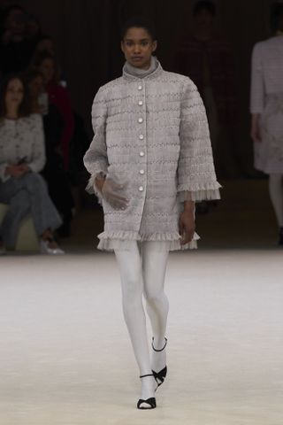 Chanel model in a gray coat minidress and gray tights at the Chanel haute couture SS24 show.