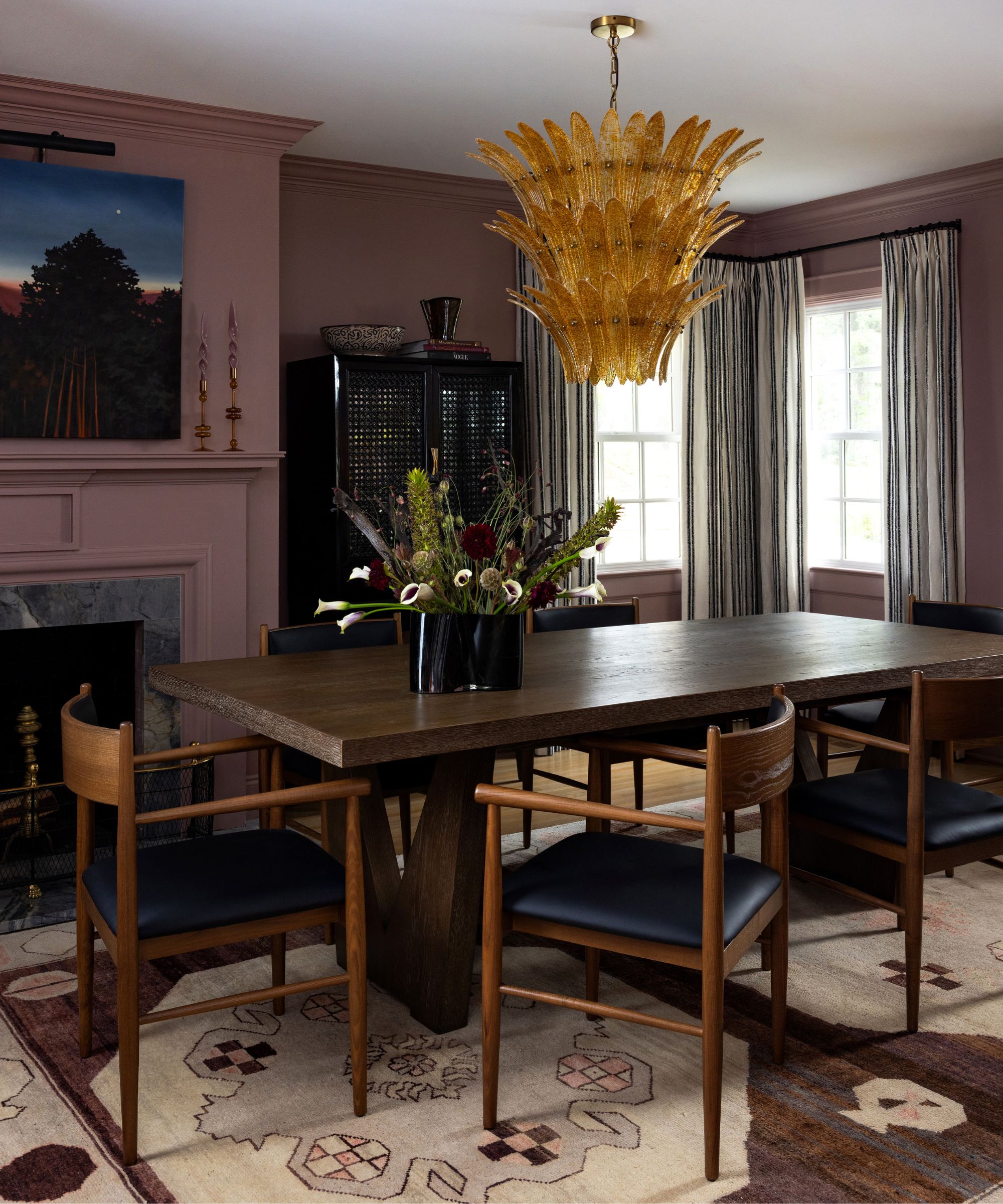 A dining room with dark mauve walls, a large dark wooden dining table and chairs, and a neutral rug on the ground.