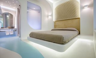 A futuristic hotel bedroom with a bed, bed under lights, wooden patterned headboard and curve patterned floor with view into the bathroom.