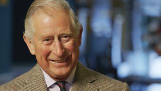 King Charles III in a tweed jacket and striped tie smiles at the camera in A Royal Grand Design.