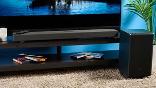 the Sharp 3.1.2 HT-SBW53121 Soundbar in black with a remote, subwoofer, against a blue background next to a panasonic TV