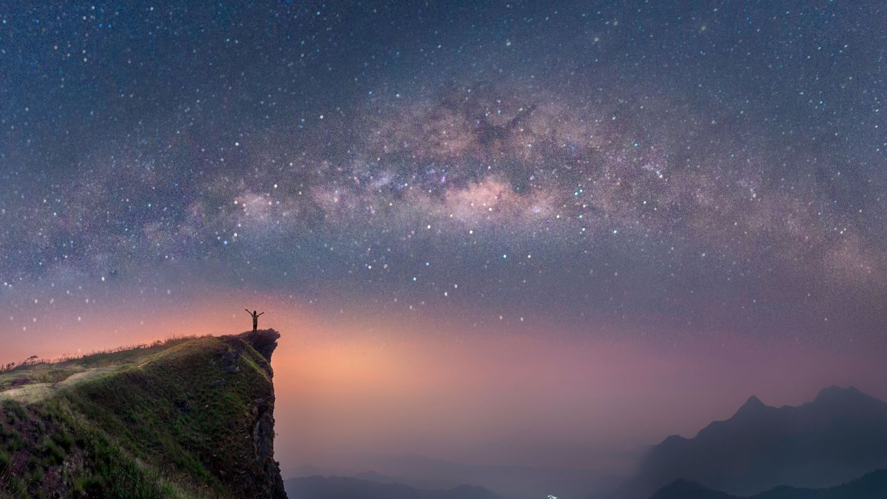 a starry night sky with a mountain in the foreground