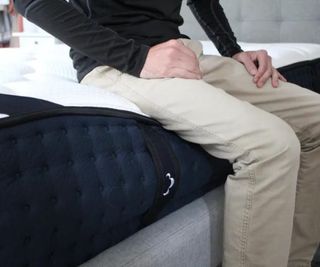 A man sitting on the side of the DreamCloud Luxury Hybrid Mattress.
