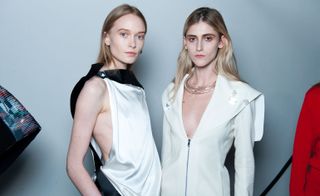 Models wearing white & black dress and a white coat with a low neckline, from Thomas Tait A/W 2015 collection.