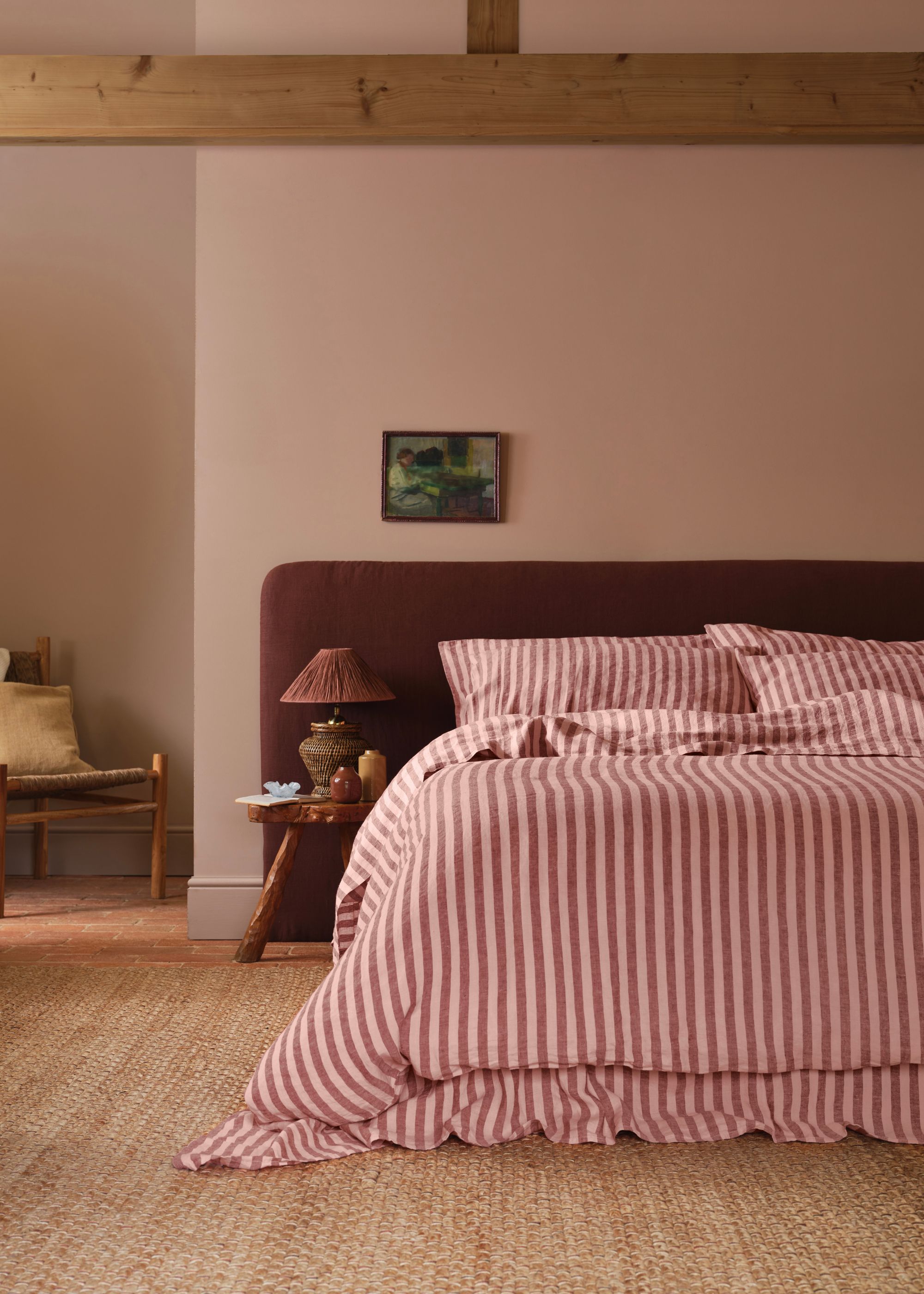 A bedroom with plaster pink walls, jute carpet, and a minimalist bed with pink striped bedding and pillows.